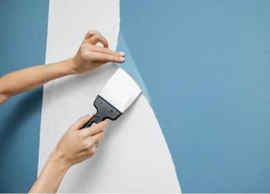 Wallpaper removal in progress using scraper on painted blue wall